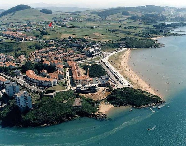 An aerial view of a coastal town with a beach, a fortified structure, and surrounding greenery. - Beachfront apartment with pool 200m and paddle tennis court (Mogro)