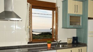 A kitchen with a view of the sea, a stove, a sink, and cabinets.