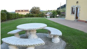 A stone outdoor table with a central round top and four attached square benches, set on a gravel surface in a landscaped garden area.