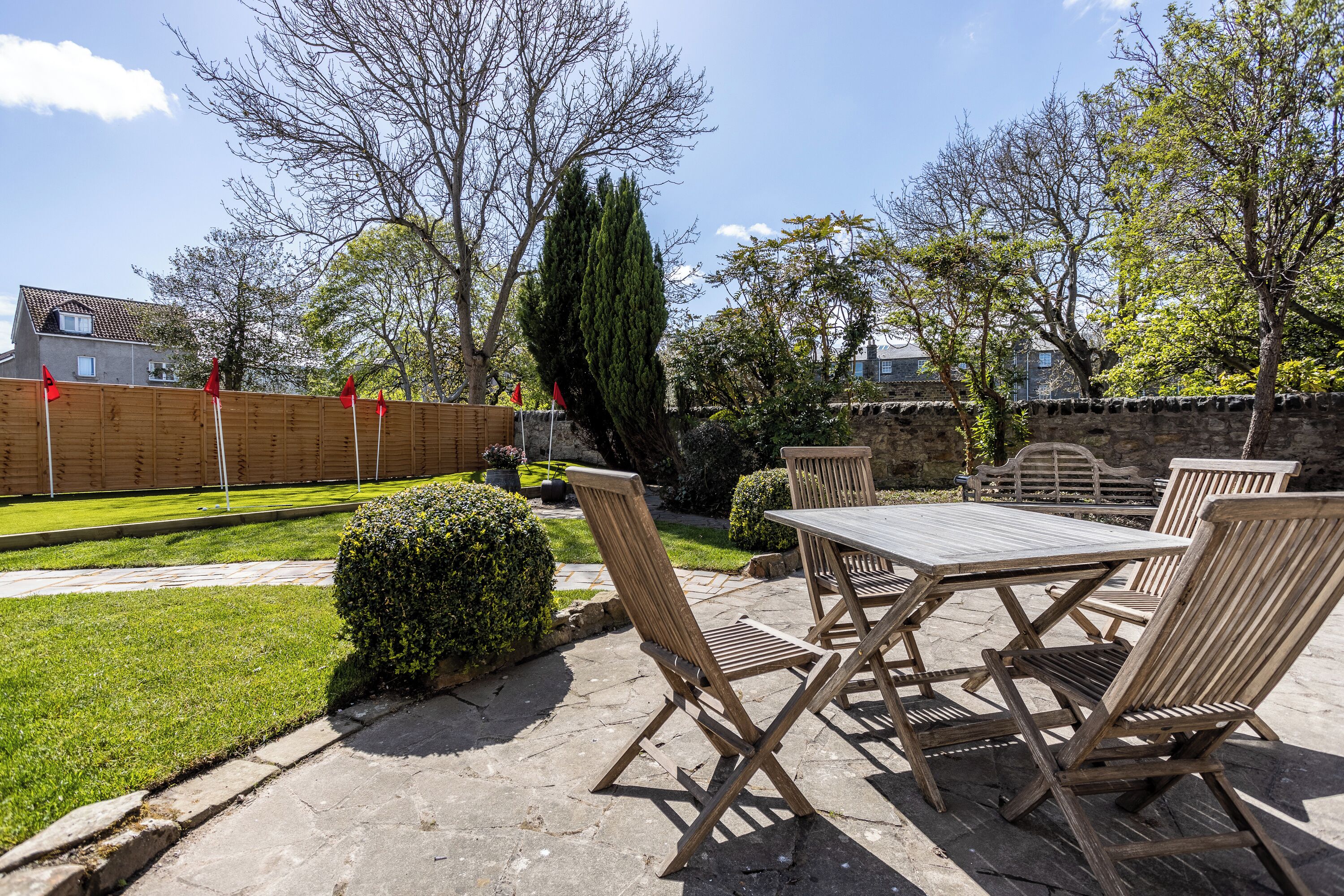 Une terrasse extérieure avec une table et des chaises en bois, entourée d’un mur de pierre et d’une clôture en bois.