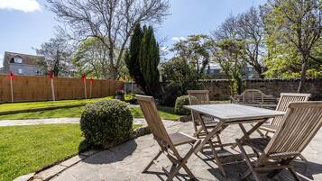 Une terrasse extérieure avec une table et des chaises en bois, entourée d’un mur de pierre et d’une clôture en bois.