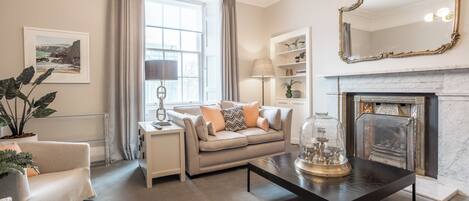 A living room with a beige sofa, a coffee table, a fireplace, and a large mirror.
