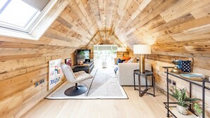 A cozy attic room with wooden walls, a sofa, a chair, a TV, and a lamp.