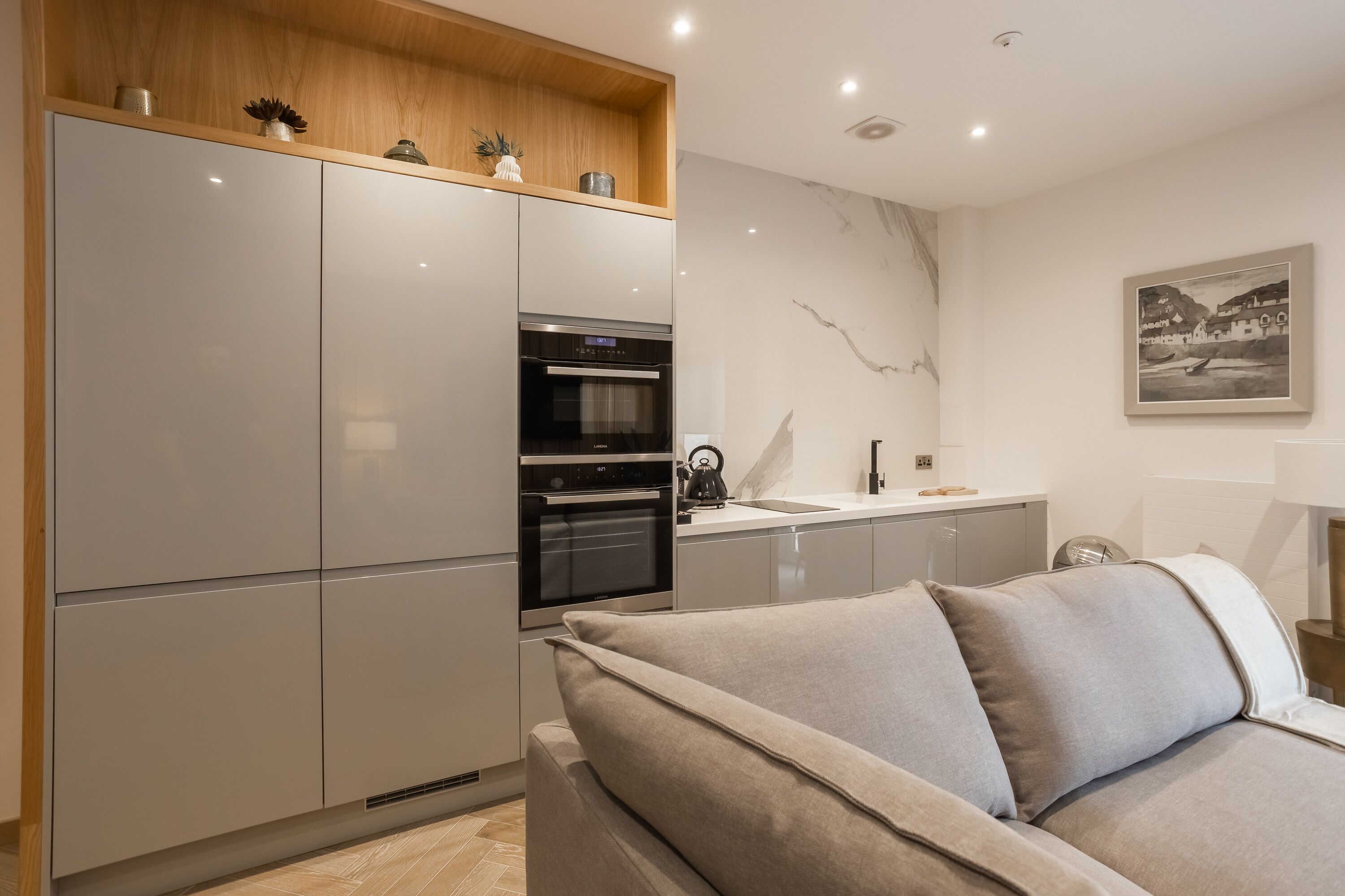 A modern kitchen with built-in appliances, a wooden shelf with decorative items, and a marble backsplash.