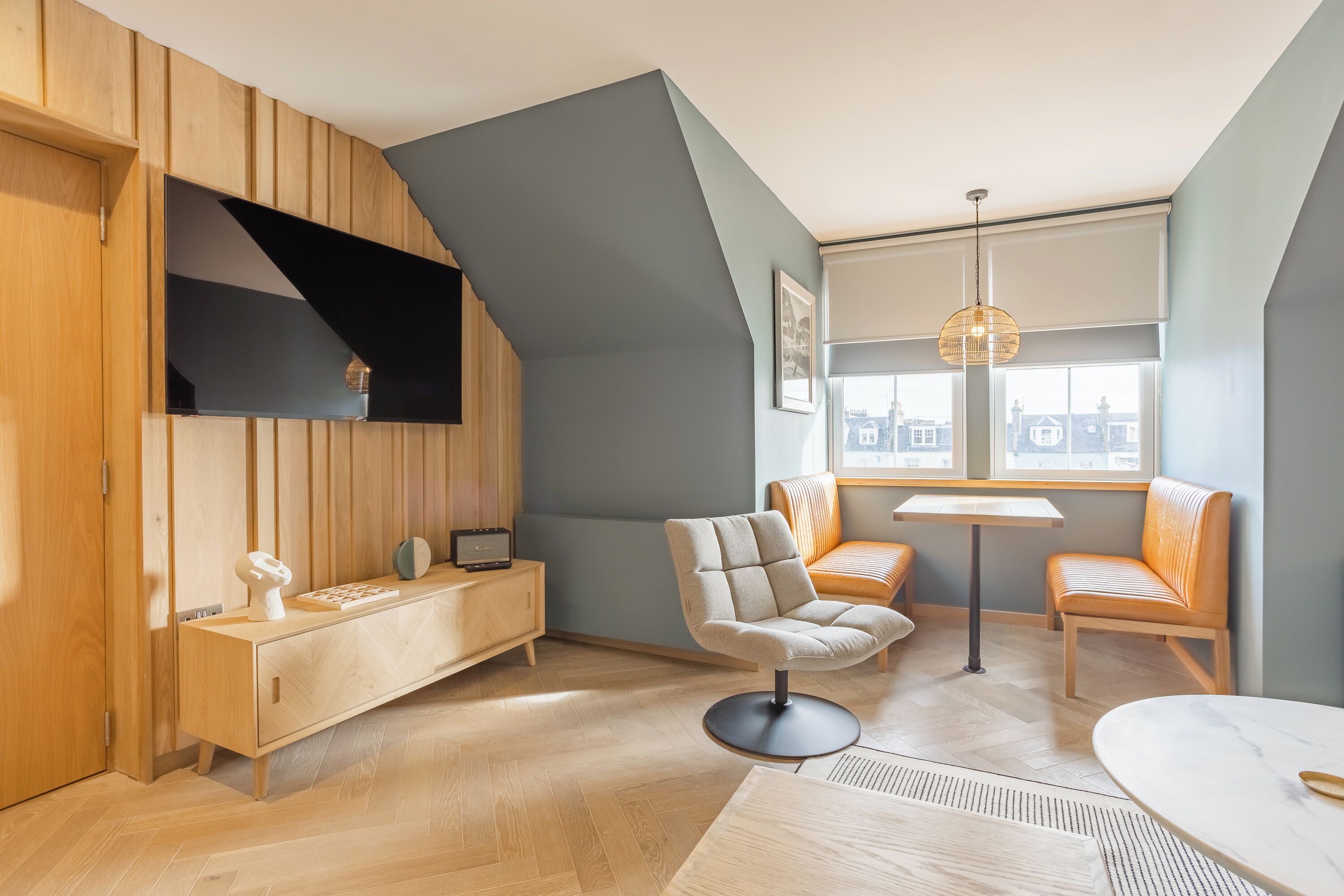 Una habitación moderna con techo inclinado, paneles de madera, televisor empotrado, una mesa redonda y dos sillones acolchados.
