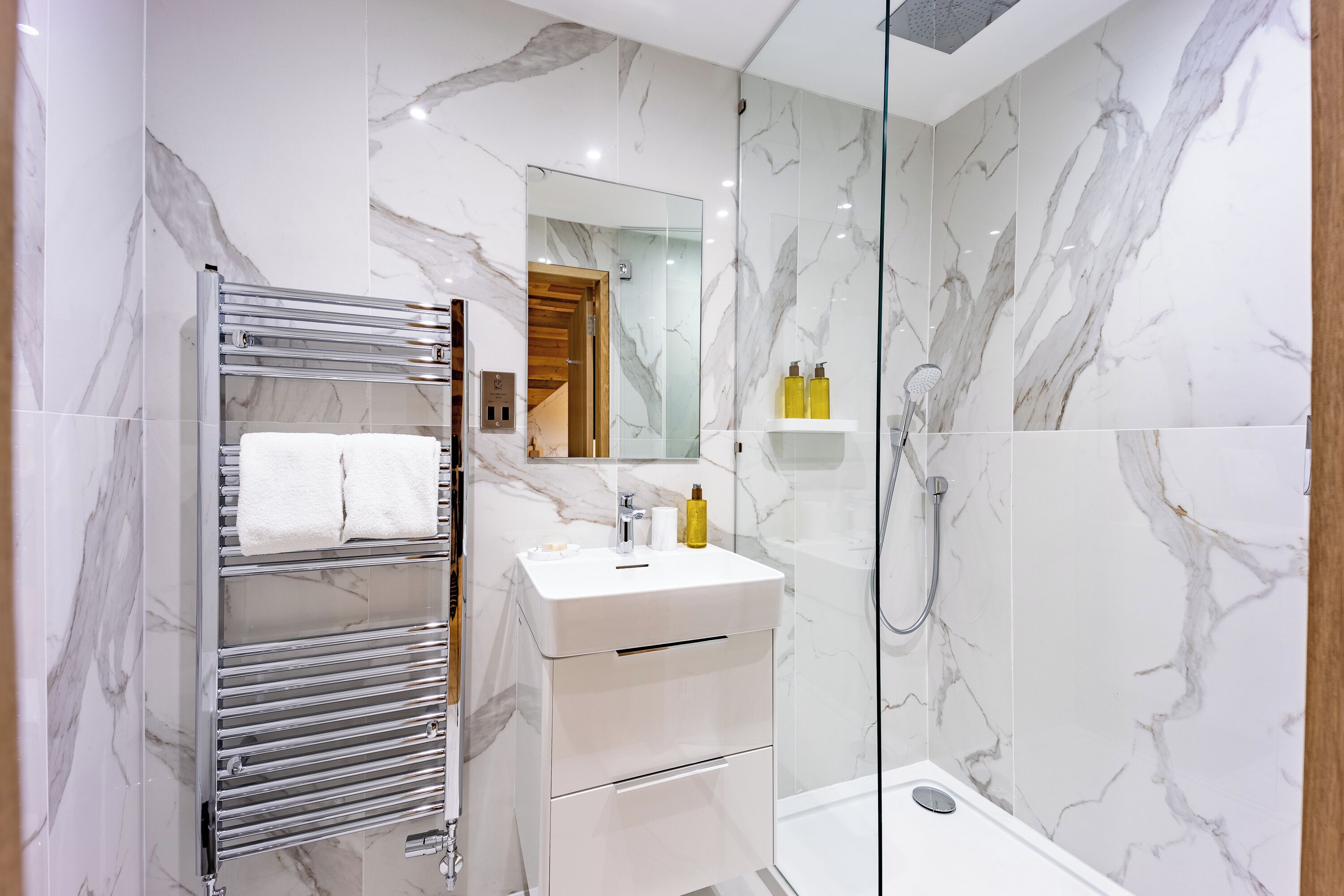 Un bagno moderno con schienale in marmo, box doccia in vetro e mobile lavabo sospeso con specchio.
