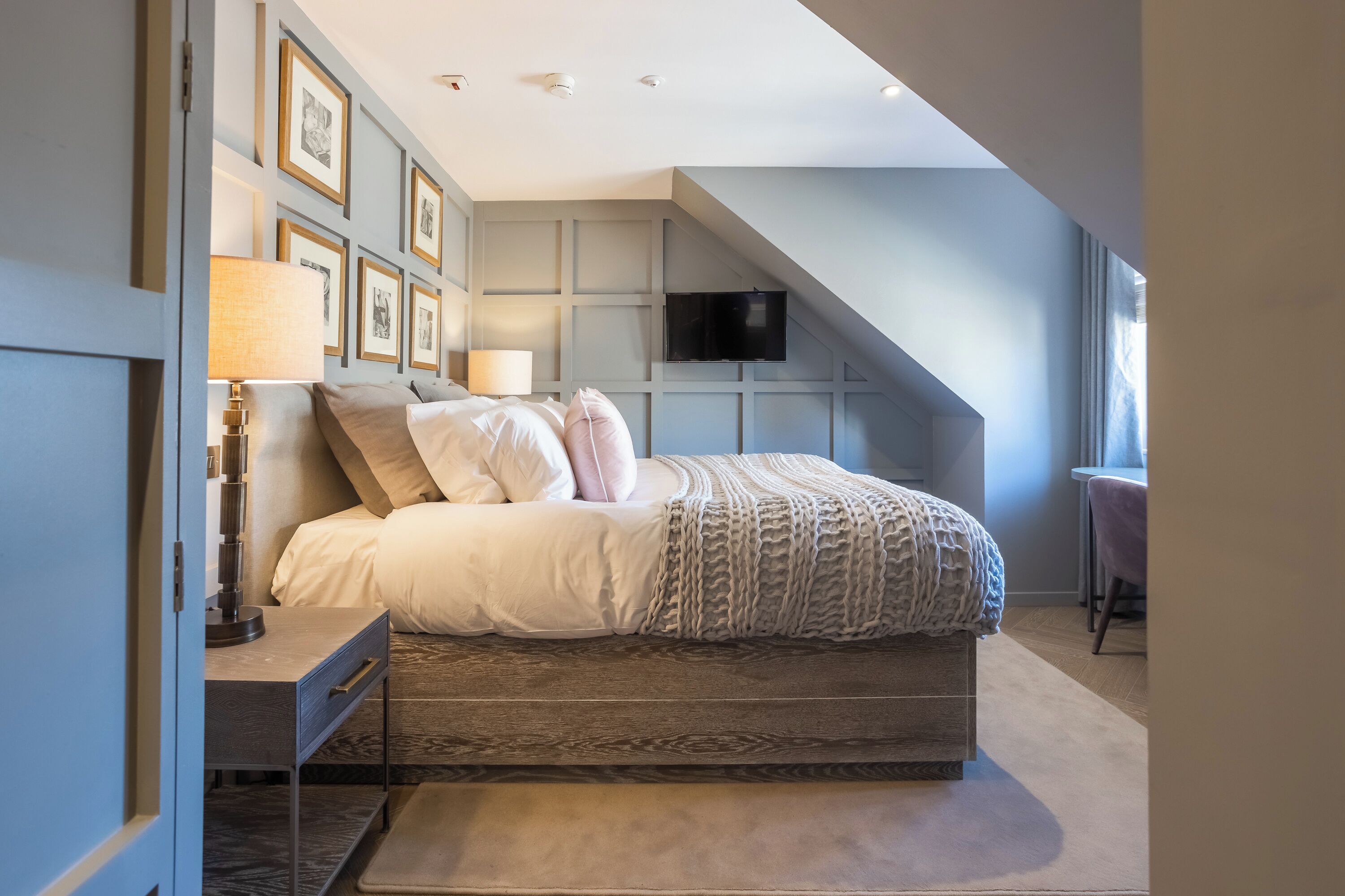 Een moderne slaapkamer met een bed, nachtkastjes, een televisie en lijstjes met foto’s aan de muur.