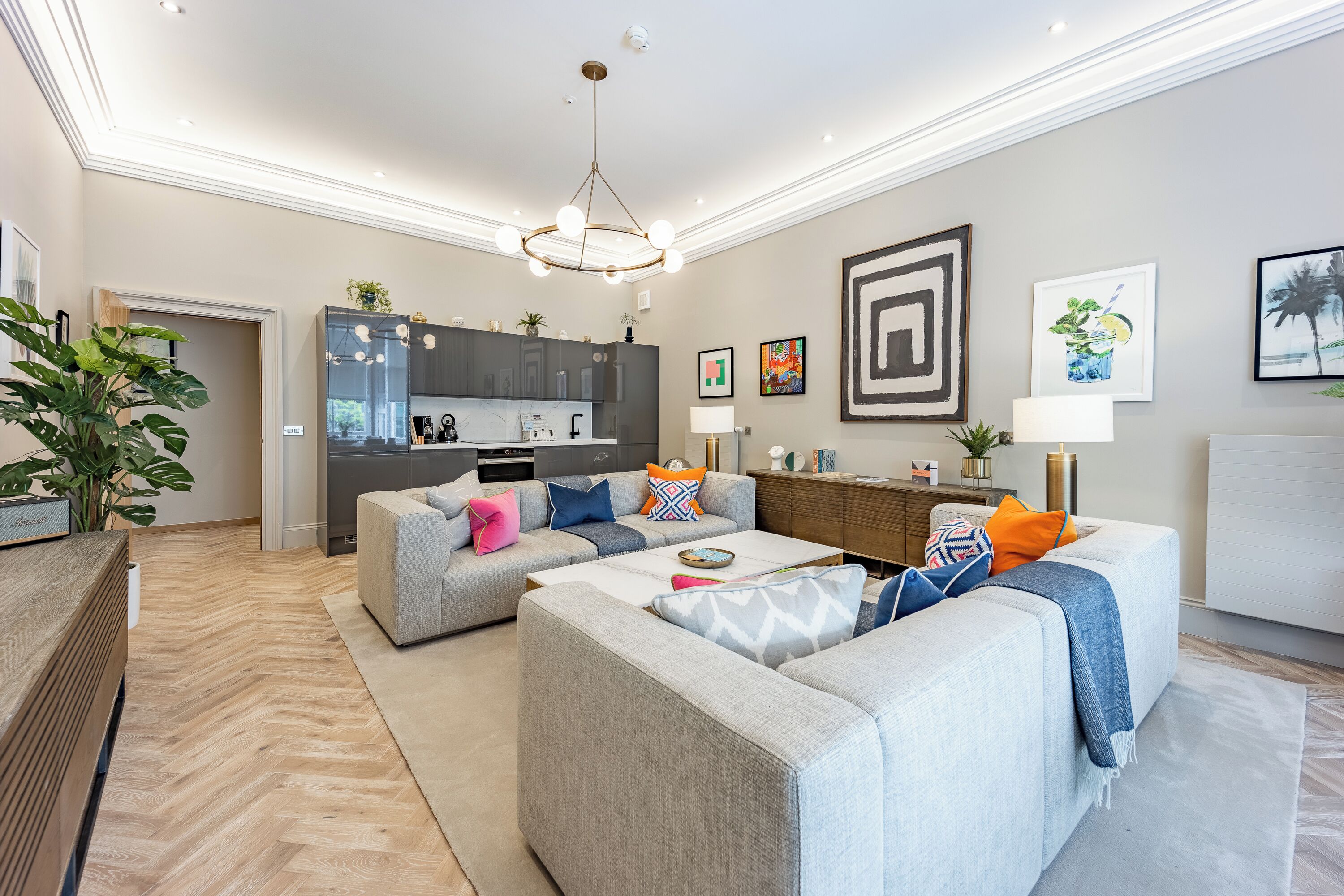 Een moderne woonkamer met een grijze zithoek, een salontafel en een keuken op de achtergrond.