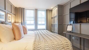 A modern hotel room with a large bed, a television on a stand, and a window with curtains.