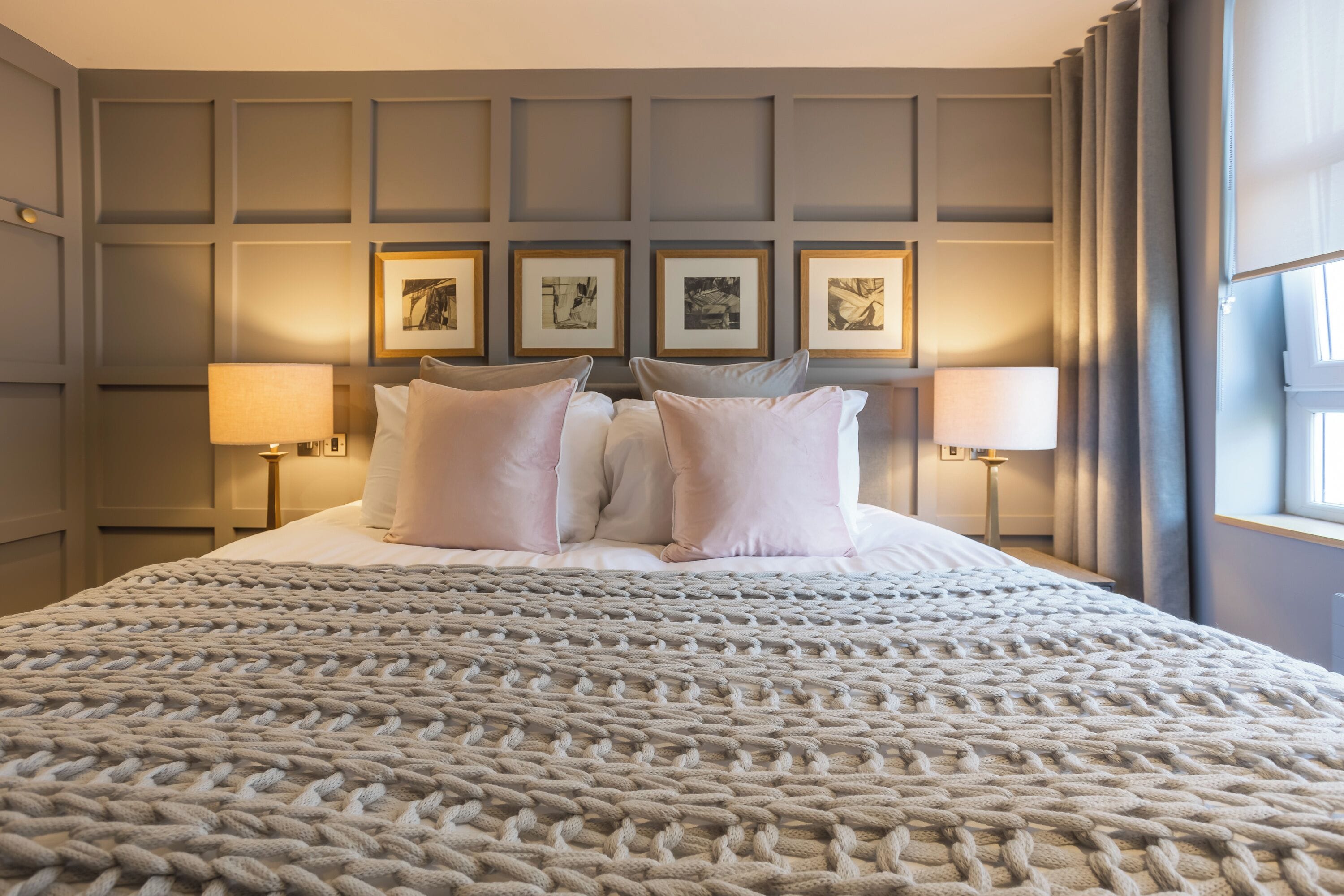 A neatly made bed with a textured blanket, two bedside lamps, and framed artwork on the wall.