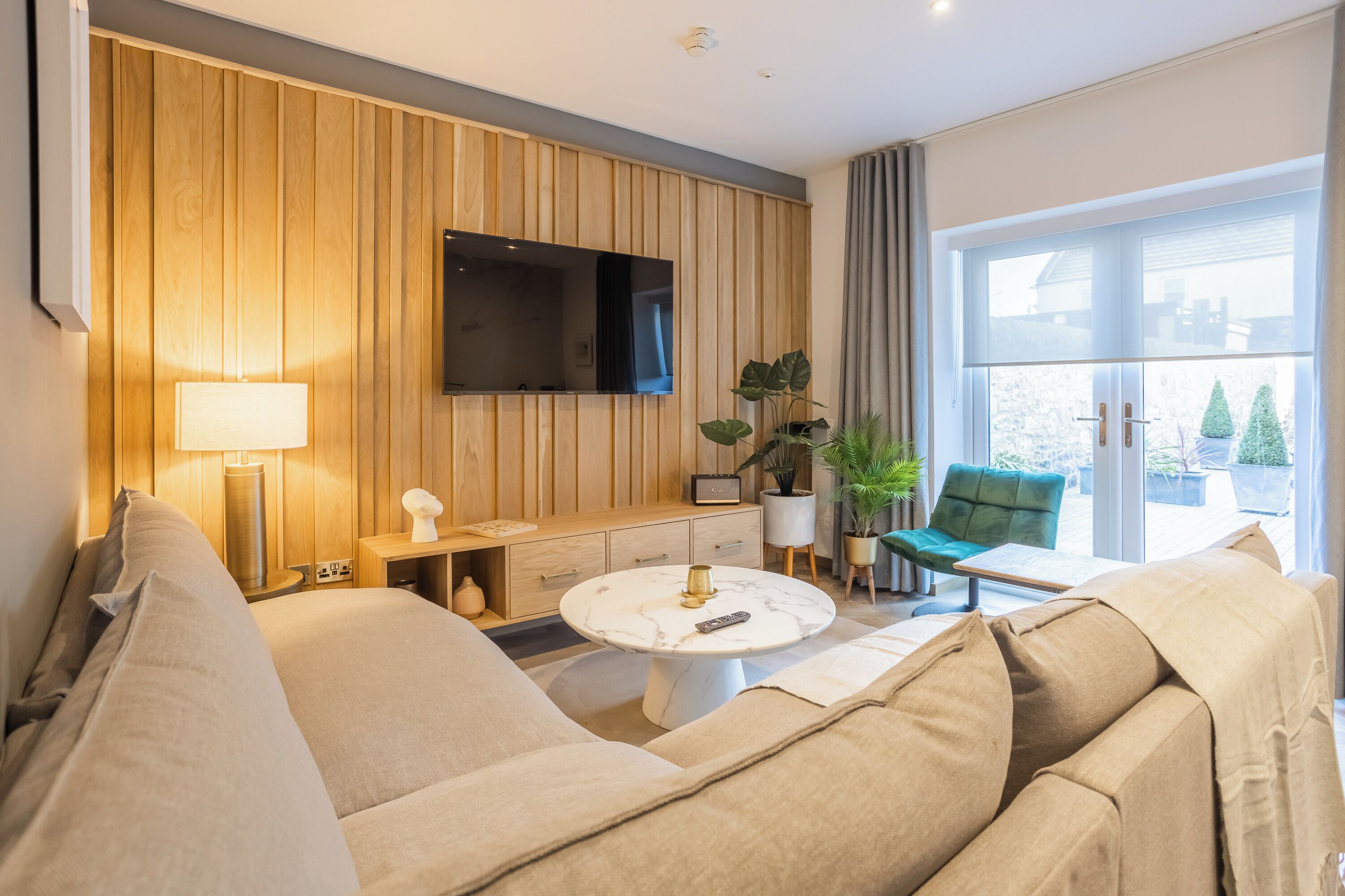 Ein modernes Wohnzimmer mit einer Couch, einem runden Couchtisch, einem an einer Holzwand montierten Fernseher und einem großen Fenster mit Blick.