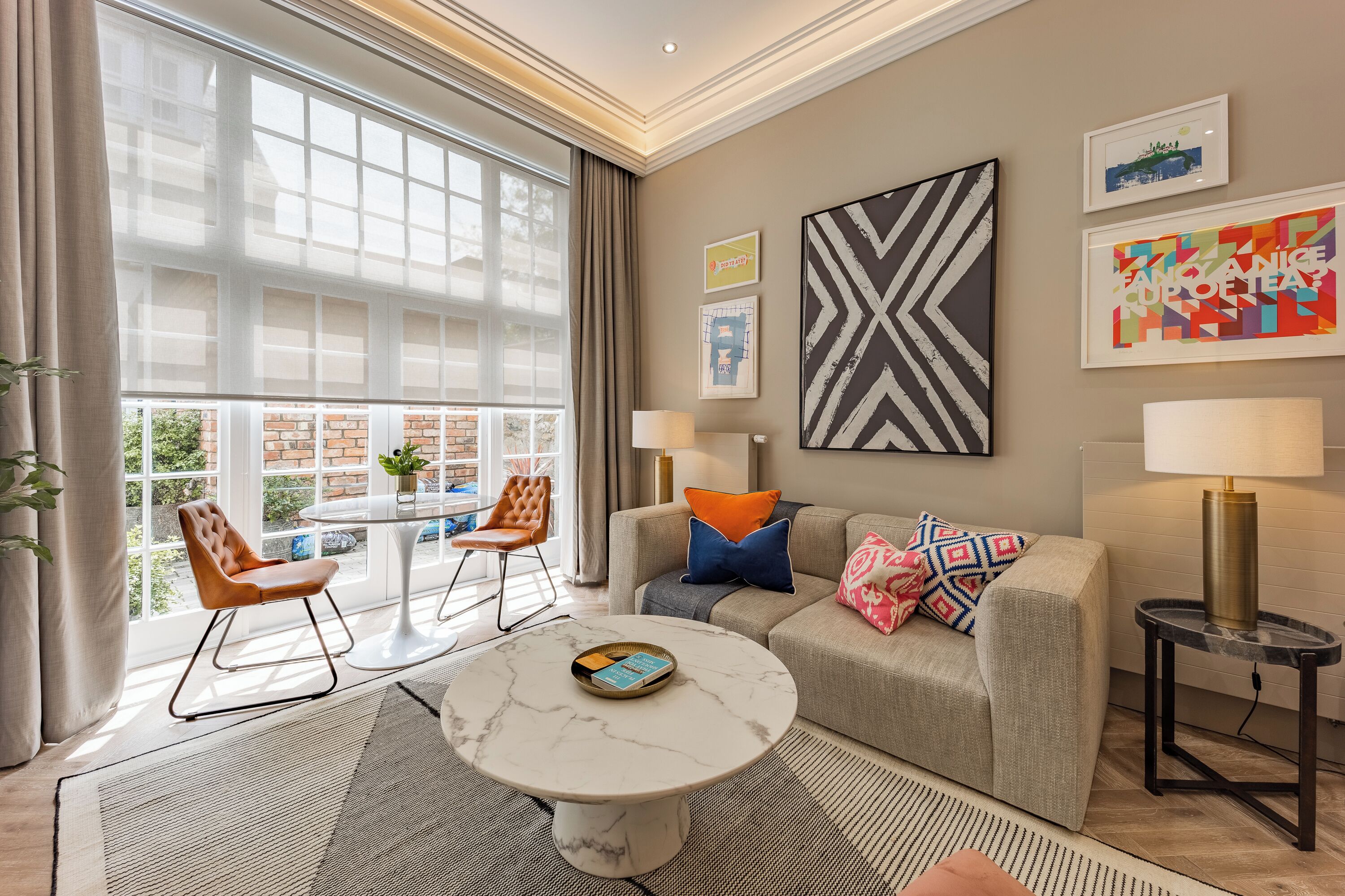 Un salon moderne avec un canapé, des fauteuils, une table basse et une vue sur un bâtiment en briques, visible à travers de grandes fenêtres.
