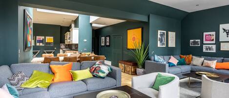 Una sala de estar moderna con un sofá seccional gris, un sillón blanco y una mesa de centro. Hay cojines de colores y una planta en maceta.