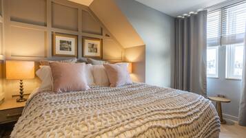 Un dormitorio con una cama grande, una mesita de noche con lámpara, un cuadro en la pared y una ventana con cortinas.