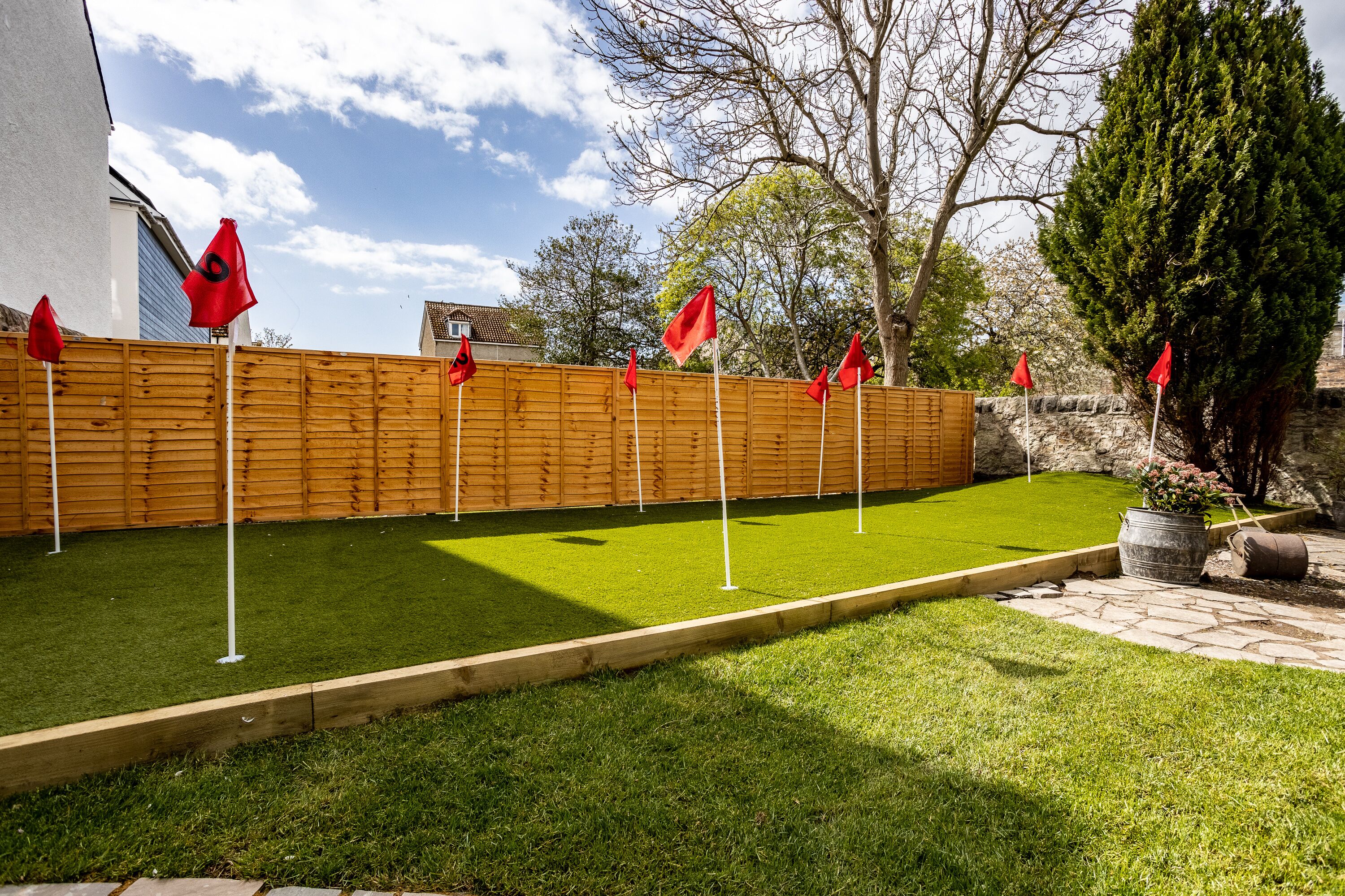 Un jardin bien entretenu, doté d’une pelouse artificielle, d’une clôture en bois et de drapeaux rouges.