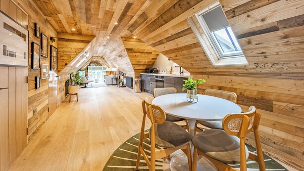 A cozy, wooden interior with a dining area, kitchen, and a loft bedroom with a skylight.
