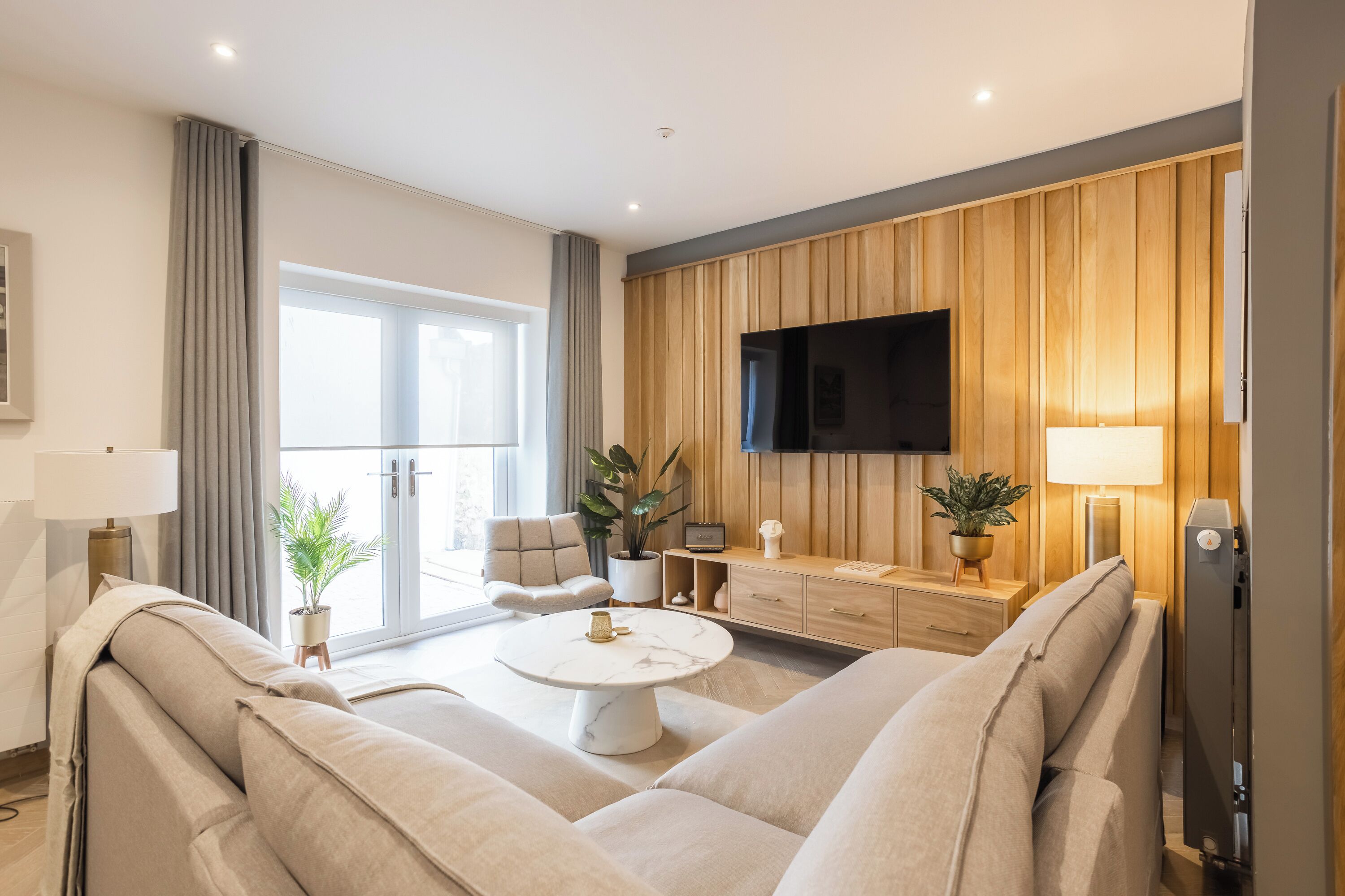 A modern living room with a sofa, a coffee table, a TV, and wooden paneling on the wall.