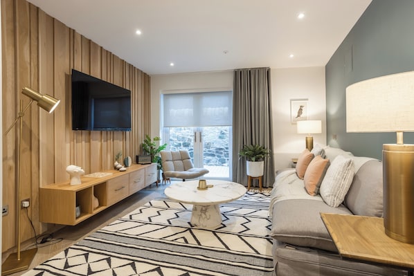 Una sala de estar moderna con un panel de pared de madera, un televisor de pantalla plana, una mesa de centro redonda, un sofá y una alfombra estampada.