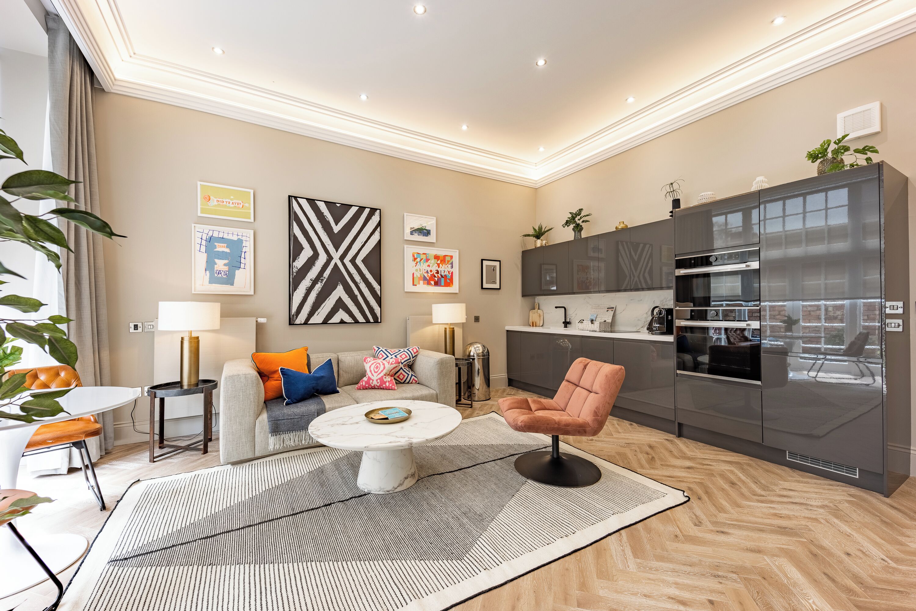 Ein modernes Wohnzimmer mit Sofa, Couchtisch und Küchenzeile mit Kühlschrank und Backofen.