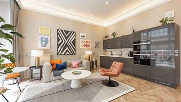 Ein modernes Wohnzimmer mit Sofa, Couchtisch und Küchenzeile mit Kühlschrank und Backofen.