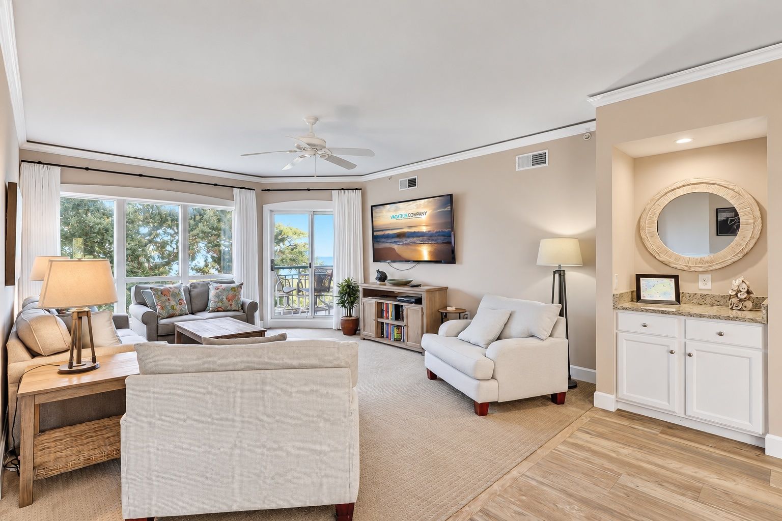 A spacious living room with a large window, a ceiling fan, a flat-screen TV, a sofa, a coffee table, and a fireplace.