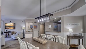 A dining area with a wooden table, white chairs, and a modern pendant light. - 3305 Windsor Court South -Amazing renovated 3rd Floor Oceanfront Villa (Hilton Head Island)