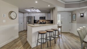 A modern kitchen with white cabinetry, a central island with stools, stainless steel appliances, and a clock on the wall. - 3305 Windsor Court South -Amazing renovated 3rd Floor Oceanfront Villa (Hilton Head Island)