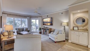 A spacious living room with a sofa, armchair, and a television mounted on the wall. - 3305 Windsor Court South -Amazing renovated 3rd Floor Oceanfront Villa (Hilton Head Island)