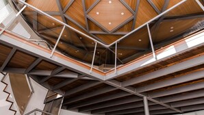 Un interior de varios niveles con un diseño geométrico en el techo, barandillas de metal y una escalera.