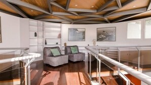Un interior moderno con techo geométrico, barandilla de vidrio y un área de descanso con sillones acolchados.