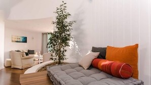Una sala de estar moderna con un sofá gris, una mesita de madera, un sillón blanco y una planta alta.