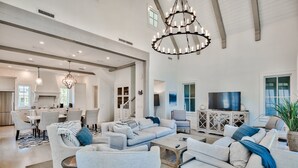 Ein geräumiges Wohnzimmer mit einer großen Eckcouch, einem Couchtisch und einem Fernseher. Es gibt eine Essecke mit Tisch und Stühlen sowie eine Küche im Hintergrund.