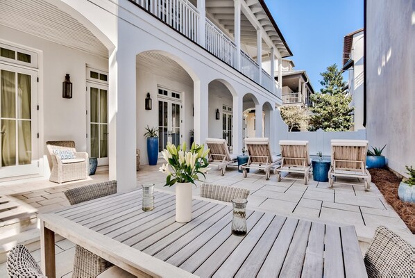 Une vaste terrasse extérieure aménagée avec du mobilier en bois, notamment une table et des chaises, ainsi qu’un grand bac à fleurs orné de fleurs blanches.