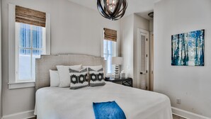 Ein Schlafzimmer mit einem großen Bett, zwei Fenstern mit Jalousien, einem Nachttisch mit Lampe, einem Bild an der Wand und einer Tür.