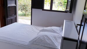 A single bed with white bedding in a room with a window and a door.