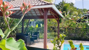 A covered outdoor area with a pool, surrounded by lush greenery and a pergola.
