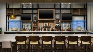 A bar area with a long counter, multiple shelves with bottles, glasses, and a large flat-screen TV. - Hilton Garden Inn Apopka City Center (Apopka)