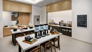 A modern breakfast area with multiple coffee stations, a chalkboard sign indicating breakfast hours, and a variety of food options. - Hilton Garden Inn Apopka City Center (Apopka)
