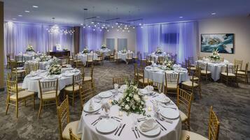 Un salón de banquetes con mesas redondas dispuestas para un evento formal, con manteles blancos, sillas doradas y centros de mesa florales.