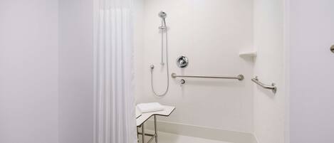 Un baño moderno con ducha, barras de apoyo, un pequeño banco y suelo de azulejos blancos.