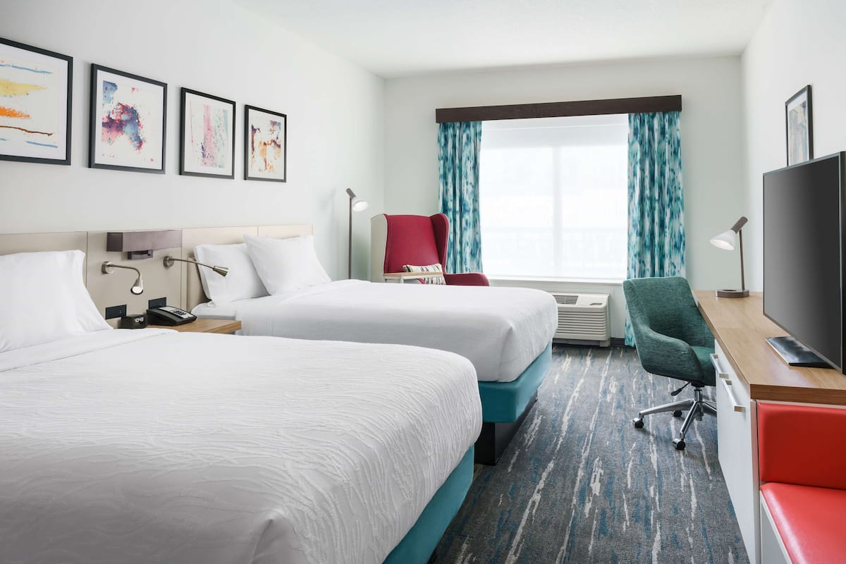 Een hotelkamer met twee bedden, een bureau met een televisie, een rode stoel en kunst aan de muur.