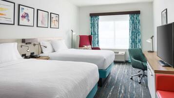 A hotel room with two beds, a desk with a TV, a red chair, and artwork on the wall.