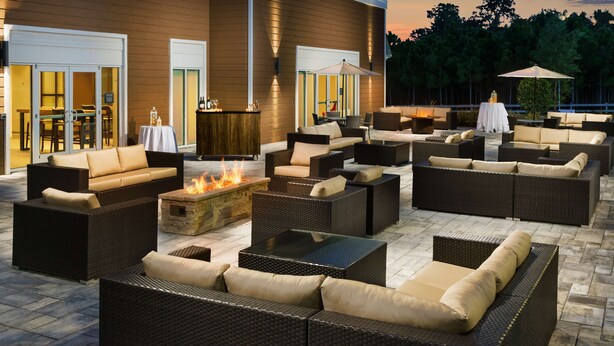 An outdoor patio with wicker furniture, a fire pit, and a view of the building's exterior. - Hilton Garden Inn Apopka City Center (Apopka)