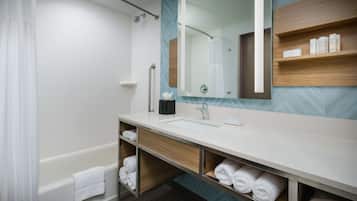 A modern bathroom with a bathtub, a large mirror, a sink, and shelves with toiletries.