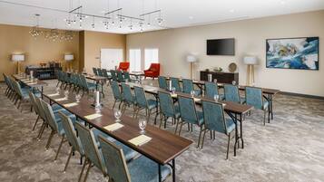 A conference room with multiple tables and chairs, a flat-screen TV, and a large abstract painting on the wall.