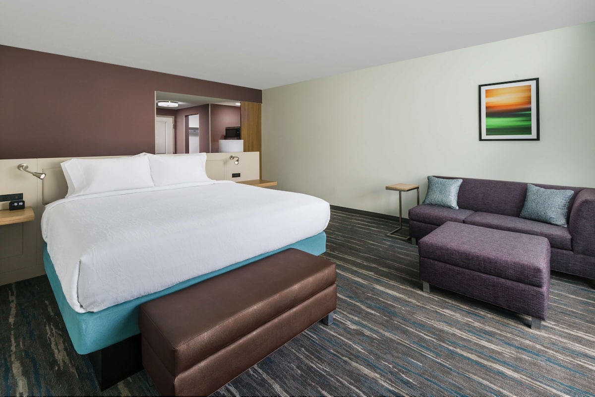 Een hotelkamer met een bed, een bankje, een slaapbank, een kleine tafel en een schilderij aan de muur.
