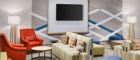 Un moderno vestíbulo de hotel con un televisor de pantalla plana grande, asientos cómodos, incluyendo sofás y sillones, y un diseño de pared con motivos.