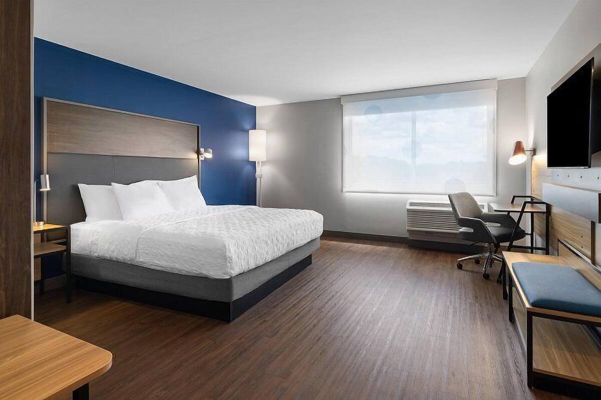 A modern hotel room with a large bed, a desk, a chair, and a TV.
