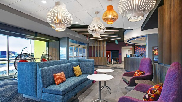 A modern lounge area with a blue sofa, purple armchairs, and a reception desk. - TRU by Hilton Perrysburg Toledo, OH (Perrysburg)
