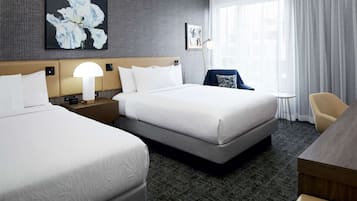 Quarto de hotel com duas camas, uma escrivaninha, uma cadeira e um abajur.